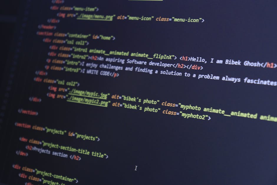 A close-up view of a person's hand typing on a silver laptop keyboard placed on a wooden table. The laptop screen displays lines of colorful code against a dark background, indicating a programming or